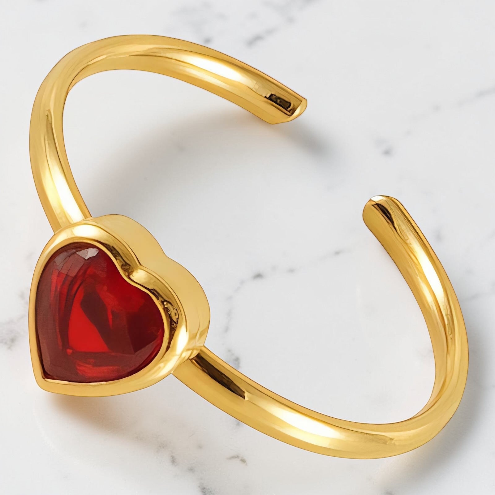 Gold open band ring featuring a deep red heart-shaped stone centerpiece