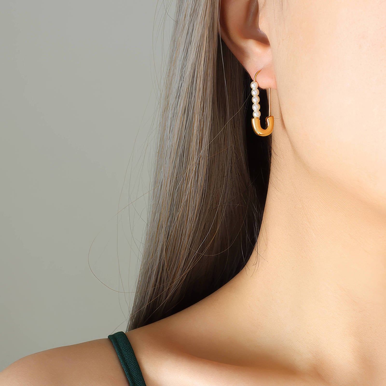 Gold-toned pearl drop earrings with an elongated curved design and French hook closure on model