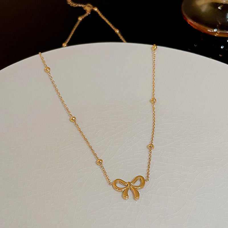 Gold bow necklace with a delicate fine chain, worn at the collarbone.