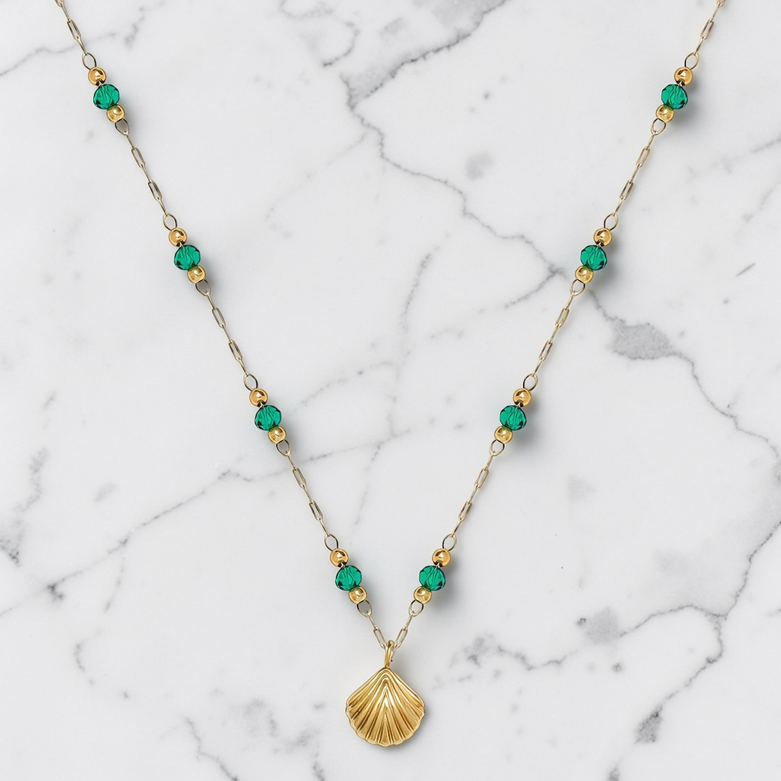 Gold beaded necklace with green accents and a shell-shaped pendant on a delicate chain