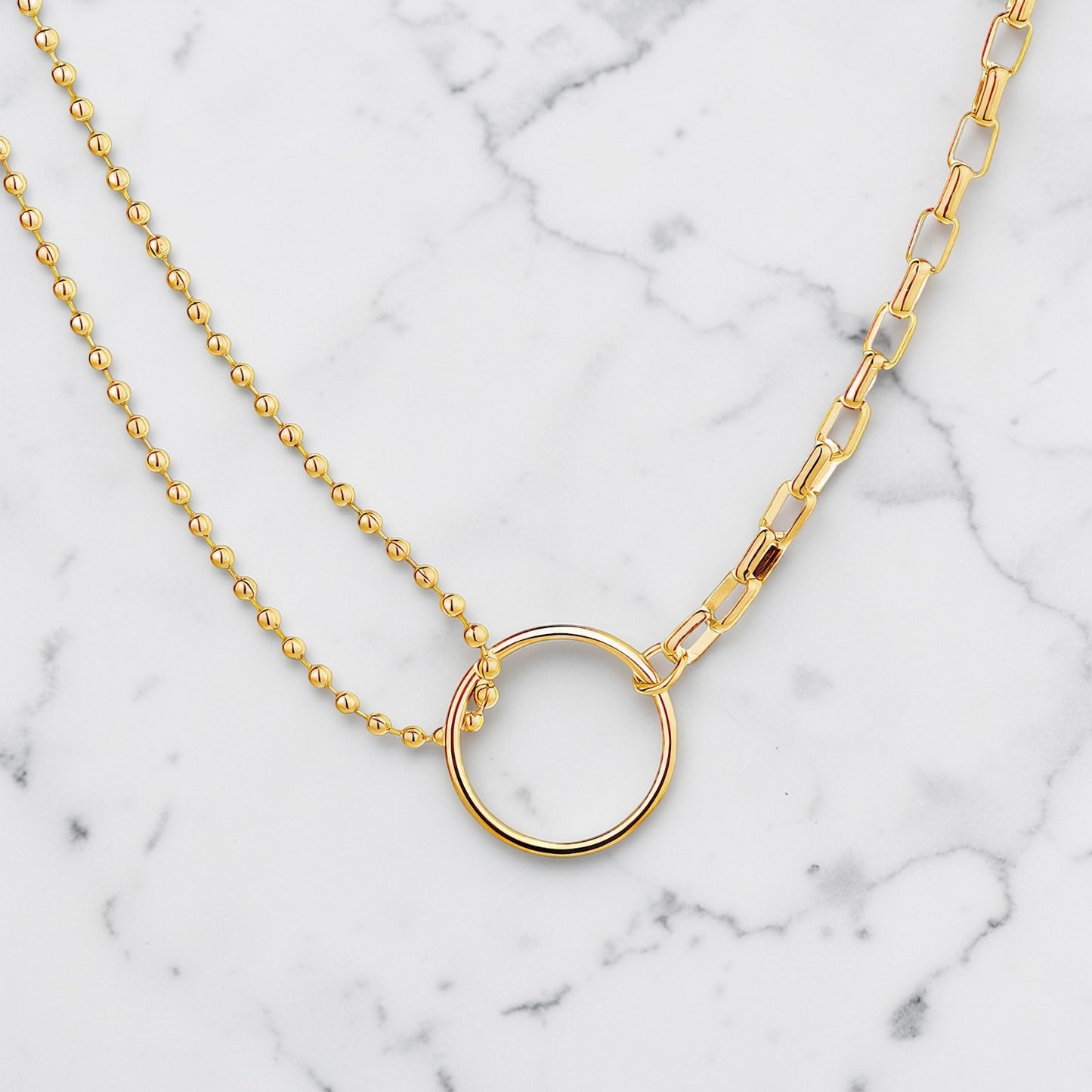Gold necklace featuring a polished open circle pendant with mixed chain design