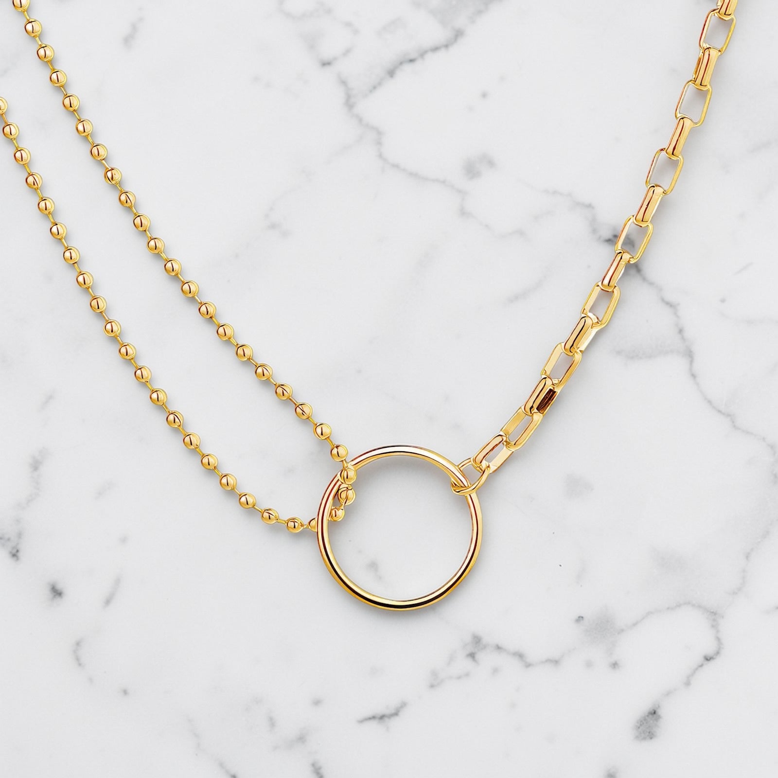Gold necklace featuring a polished open circle pendant with mixed chain design