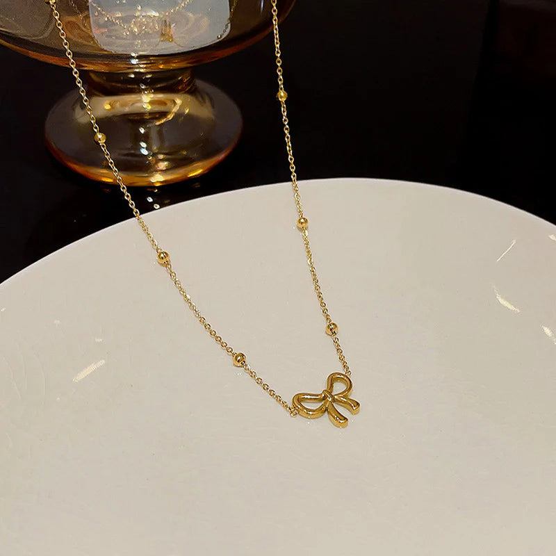 Gold bow necklace with a delicate fine chain, worn at the collarbone.