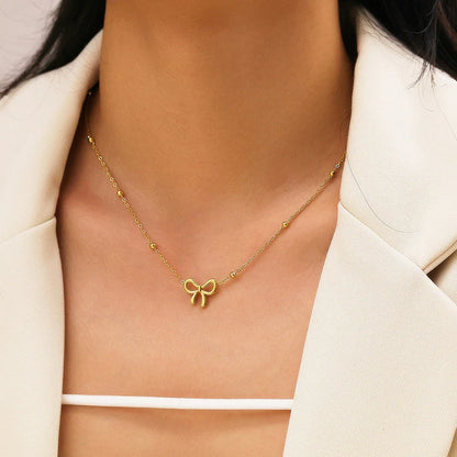 Gold bow necklace with a delicate fine chain, worn at the collarbone.