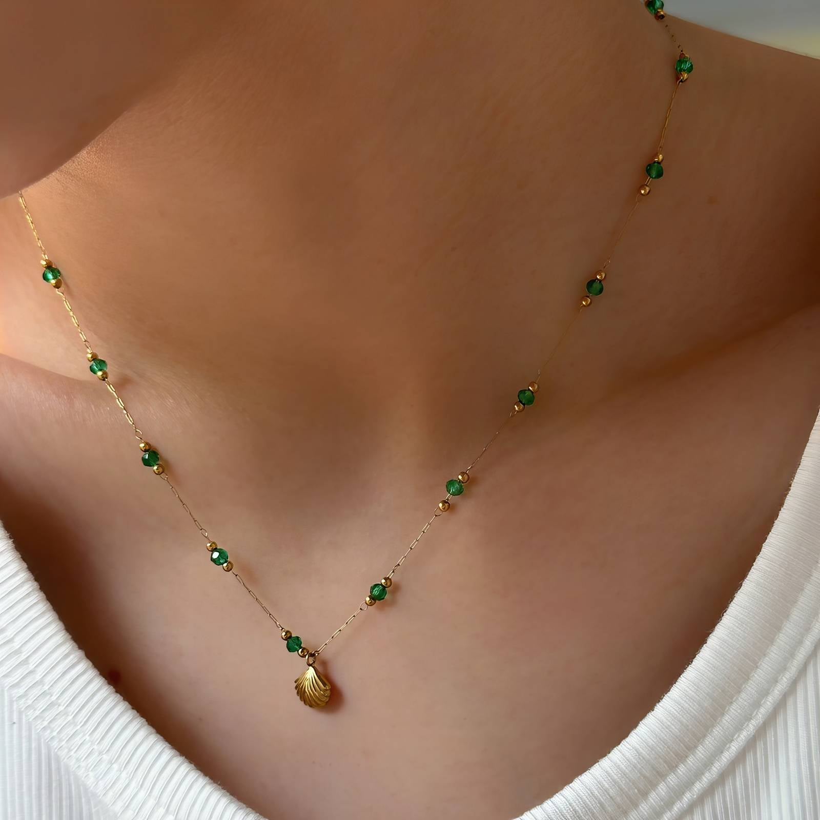 Gold beaded necklace with green accents and a shell-shaped pendant on a delicate chain