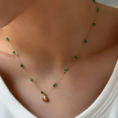 Gold beaded necklace with green accents and a shell-shaped pendant on a delicate chain